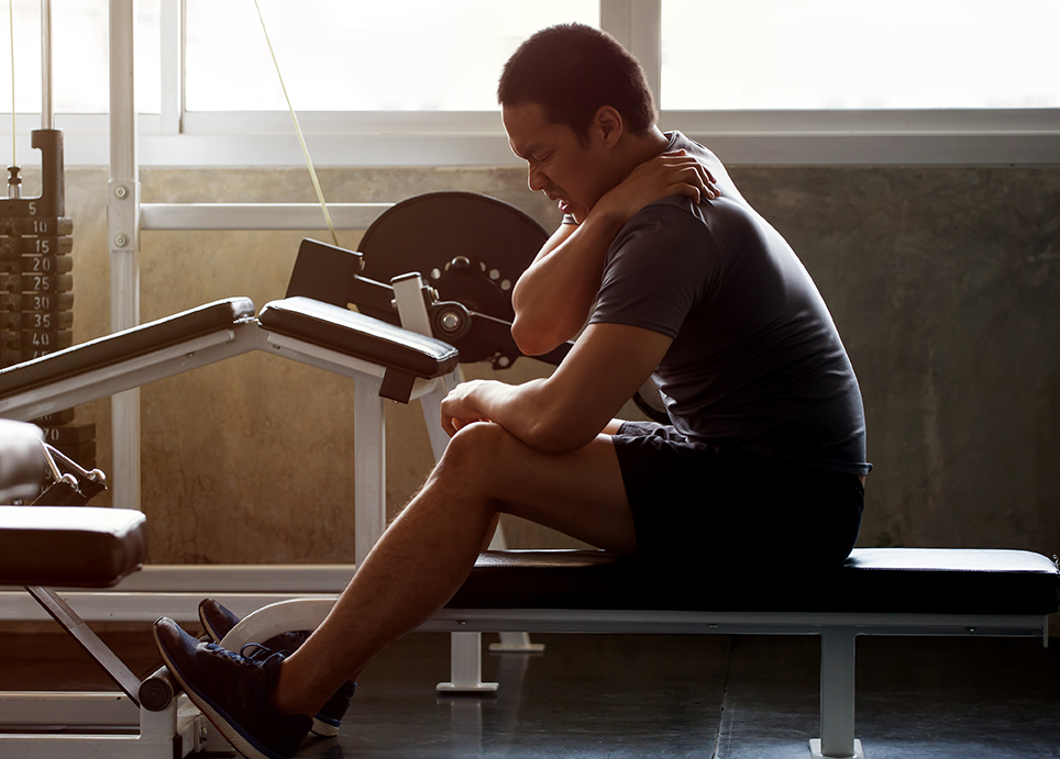 Man sitting atop a bench in a gym, experiencing neck pain